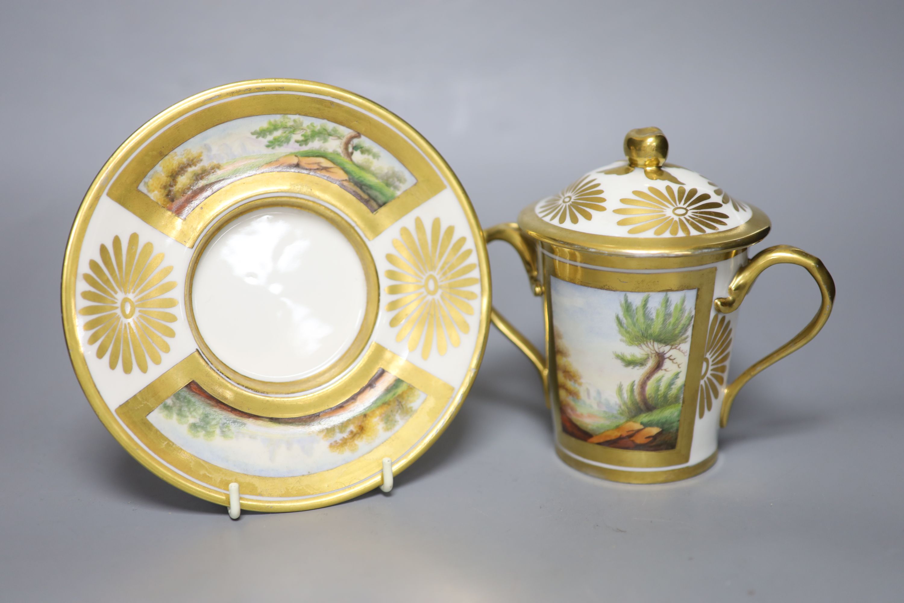 A 19th century Paris porcelain two handled chocolate cup, cover and stand painted with two landscapes in gilt panels to both the cup an